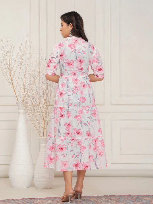 Woman wearing a floral dress standing in a room with a white wall and decorative elements.