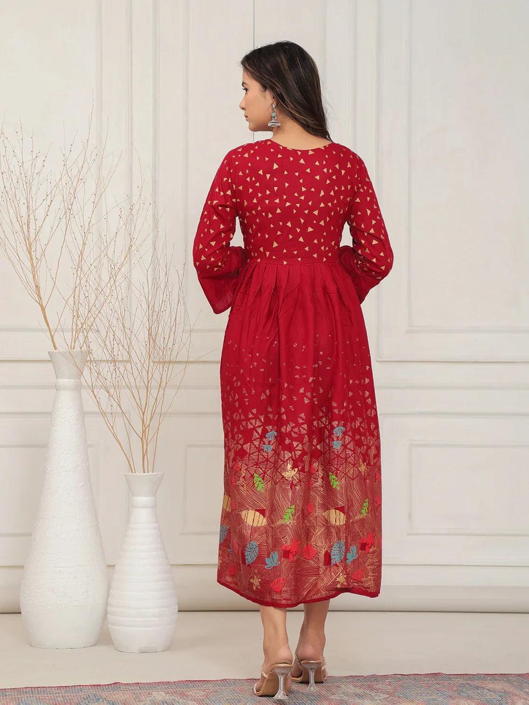 Woman wearing a red dress with floral patterns in a minimalistic setting.
