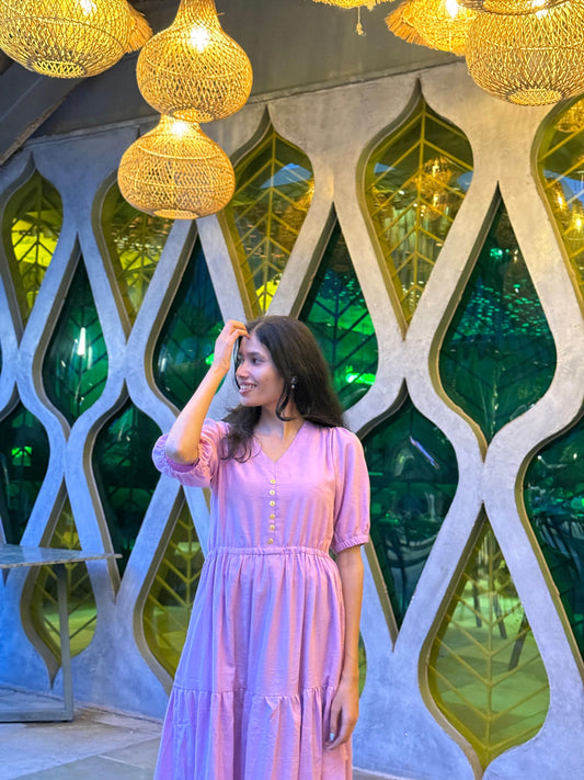Woman in a pink dress standing in front of decorative wall with geometric patterns and hanging lights.