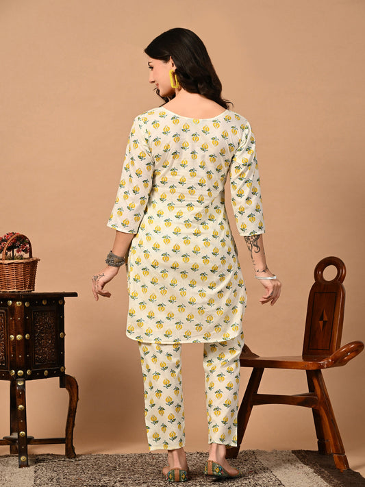 Woman wearing a white floral dress standing in front of a beige wall with a wooden chair and table.