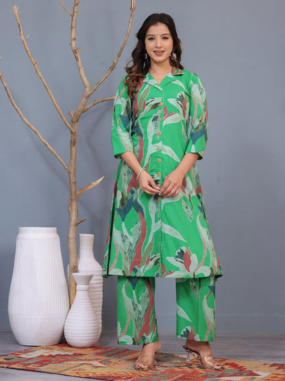 Woman wearing a green floral outfit standing in front of white vases and a gray wall. > Mitrika