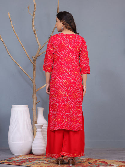 Woman wearing a red patterned outfit standing against a gray wall with decorative vases. > Mitrika