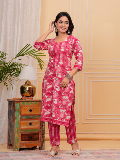 Woman wearing a pink floral kurta with pants in a room with a lamp and plant.