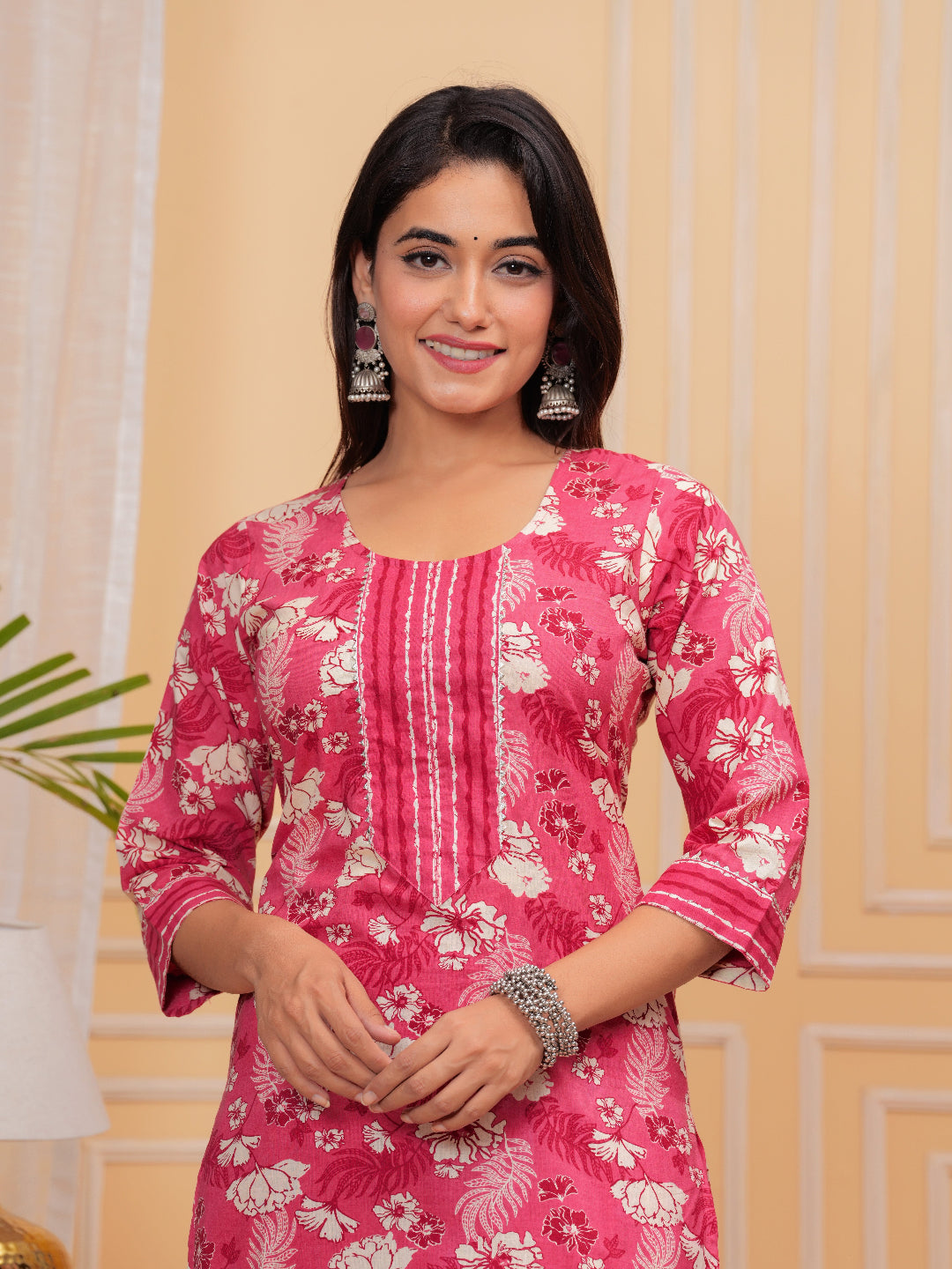 Woman wearing a pink floral dress against a beige wall.