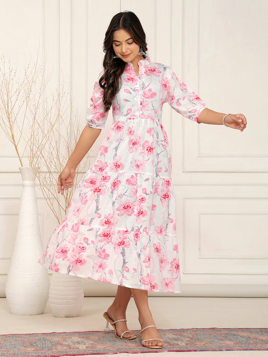 Woman wearing a floral dress standing in a room with a white wall and decorative rug. > Mitrika