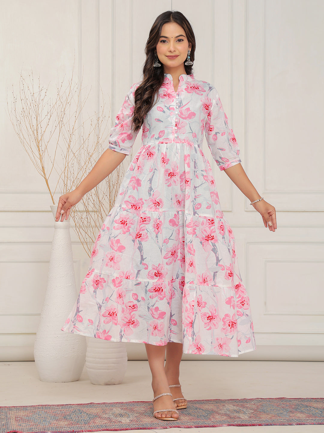 Woman wearing a floral dress standing against a white wall.