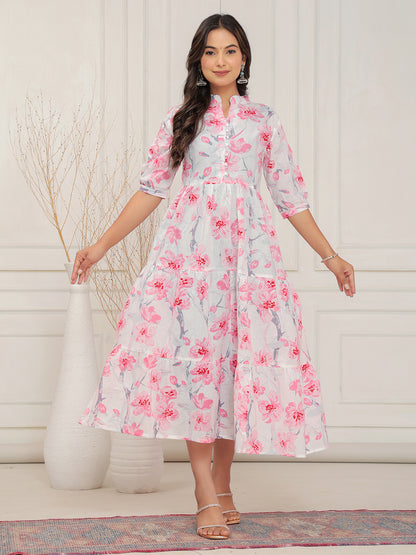 Woman wearing a floral dress standing against a white wall.