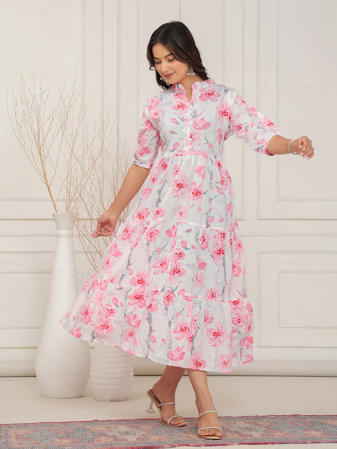 Woman wearing a floral dress standing in a room with a white wall and decorative rug.
