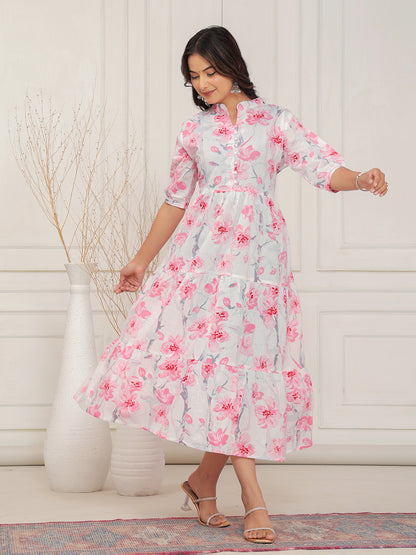 Woman wearing a floral dress standing in a room with a white wall and decorative rug.