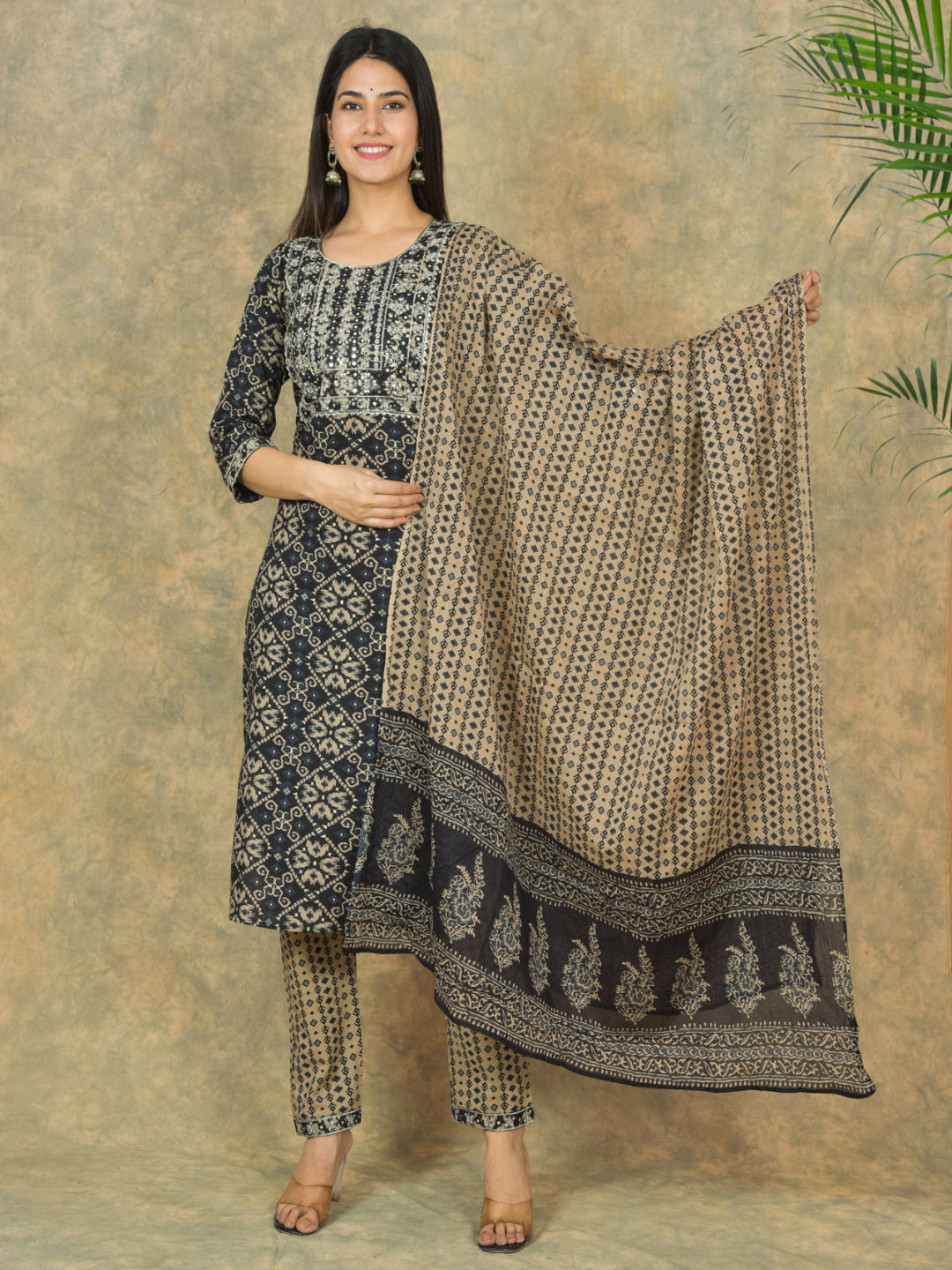 Woman holding a patterned dupatta against a textured wall