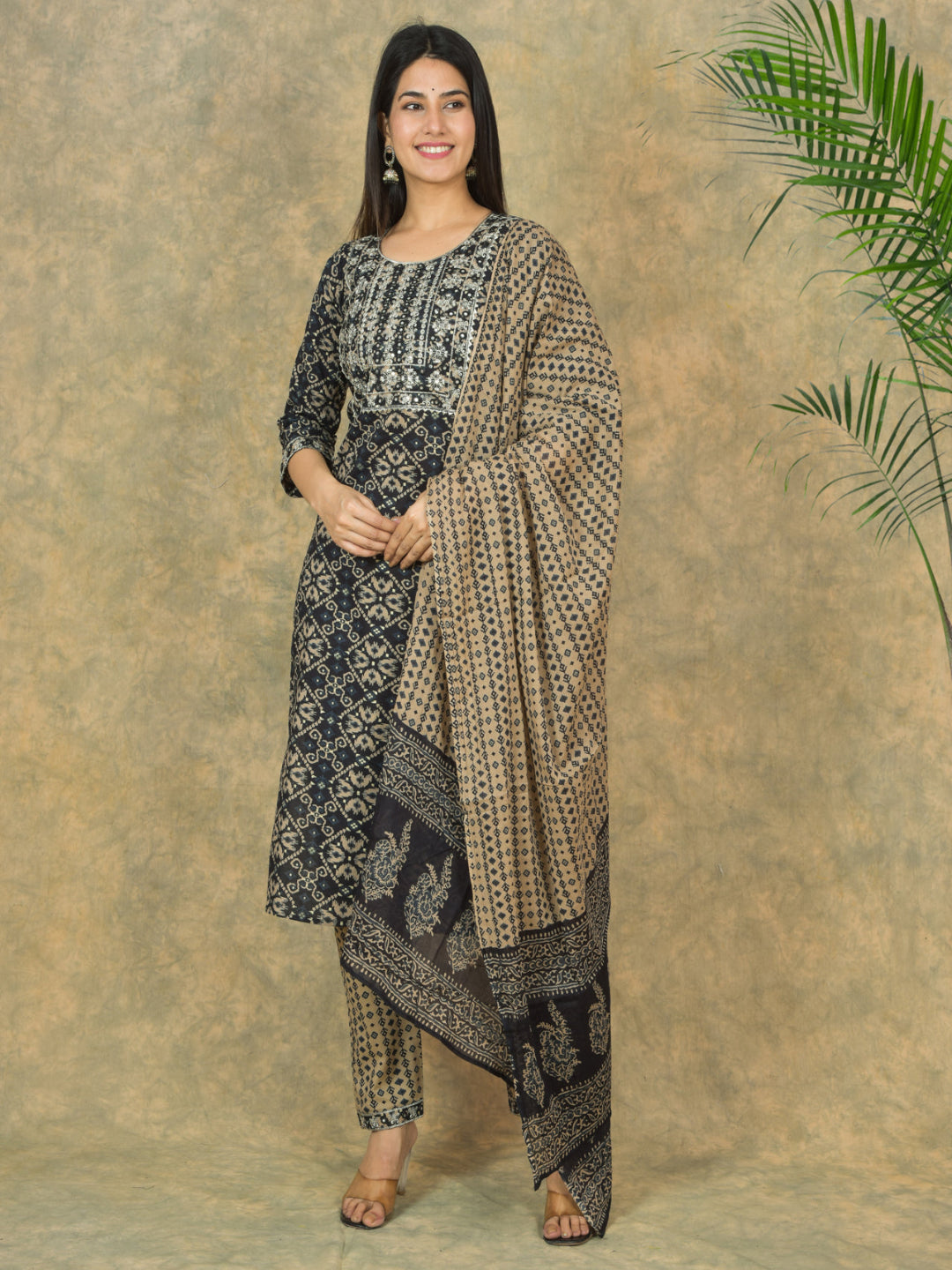 Woman wearing a traditional outfit with a patterned dress and dupatta against a beige background