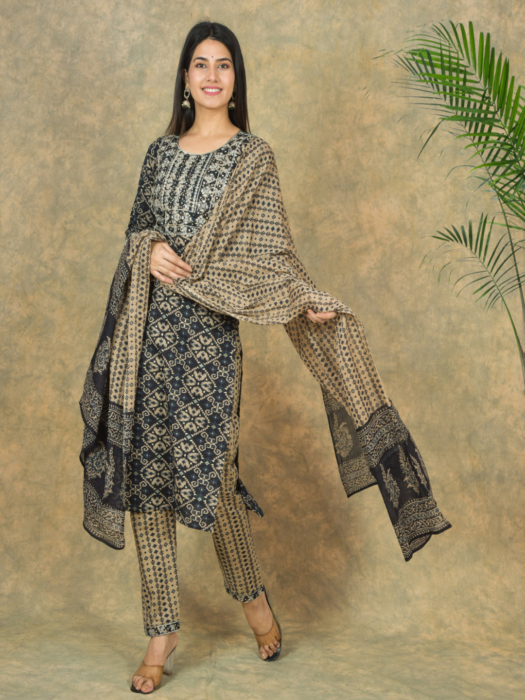 Woman wearing a traditional outfit with a patterned shawl against a textured wall.