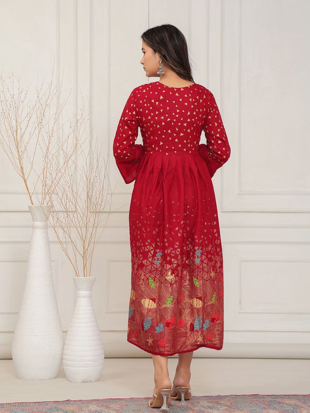 Woman wearing a red dress with floral patterns in a minimalistic setting.