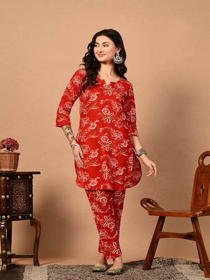 Woman wearing a red floral outfit standing against a beige background > Mitrika
