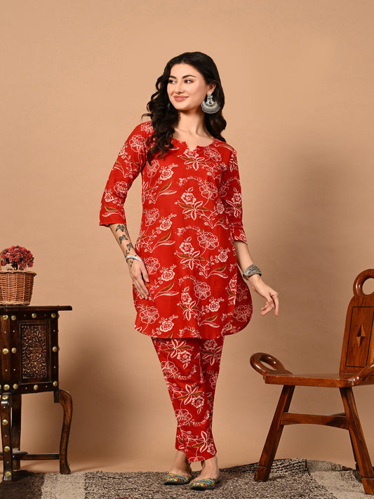 Woman wearing a red floral outfit standing against a beige background > Mitrika
