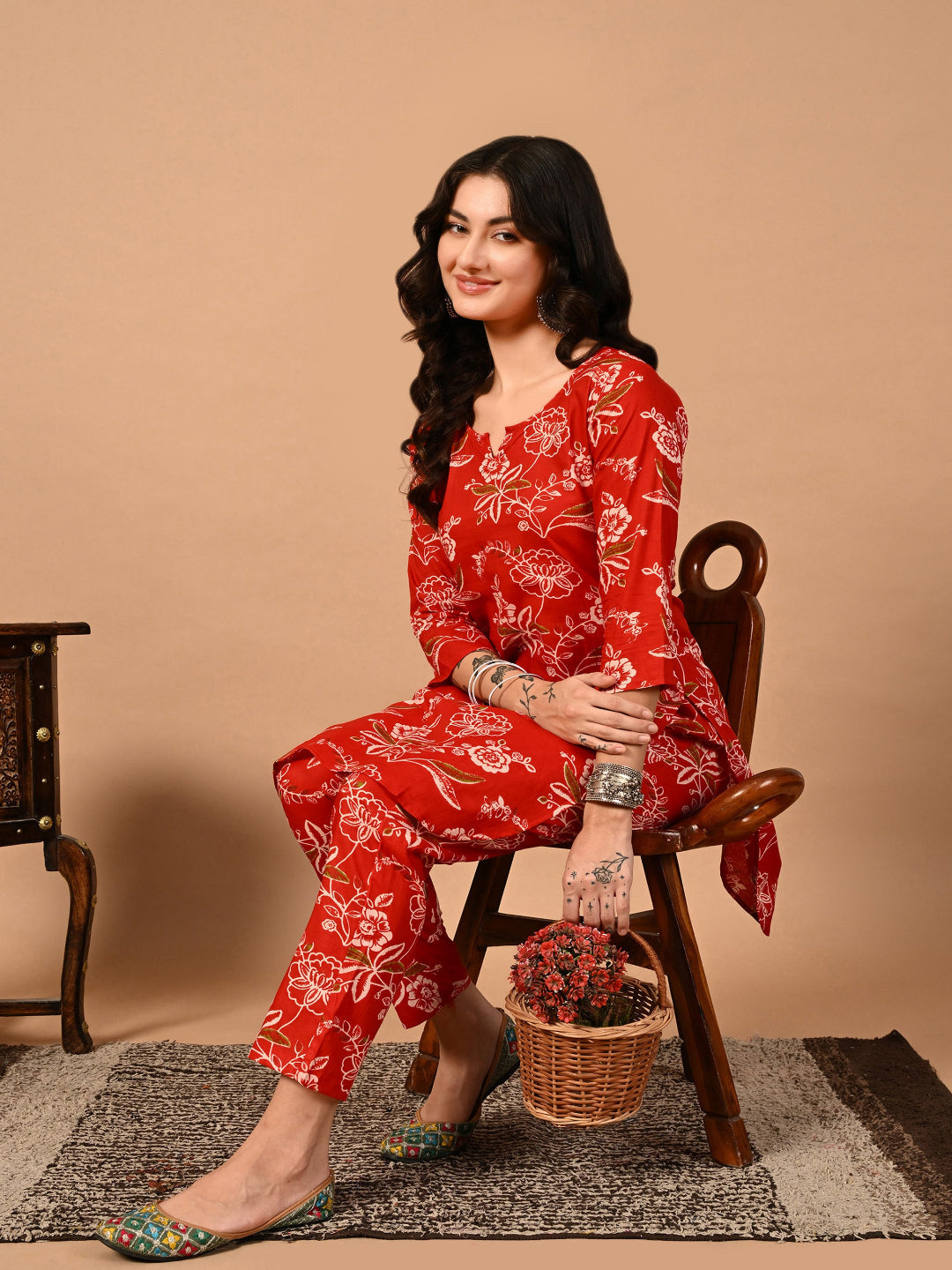 Woman in a red floral outfit sitting on a wooden chair with a beige background