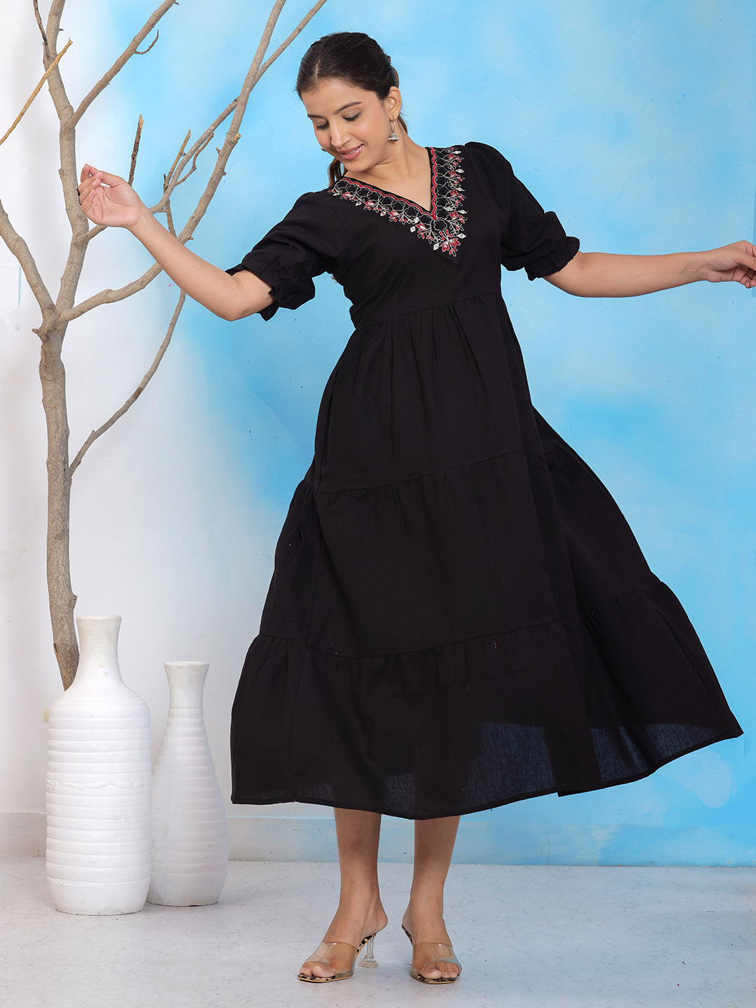 Black embroidered midi dress, V-neck tiered dress, puff sleeve black dress, solid black cotton dress, casual black summer dress, embroidered neckline dress, elegant black midi dress, boho style black dress, 3/4 sleeve A-line dress, festive black dress, flowy solid dress, party wear black midi dress, statement black outfit, embroidered casual dress, ethnic fusion black dress. > Mitrika