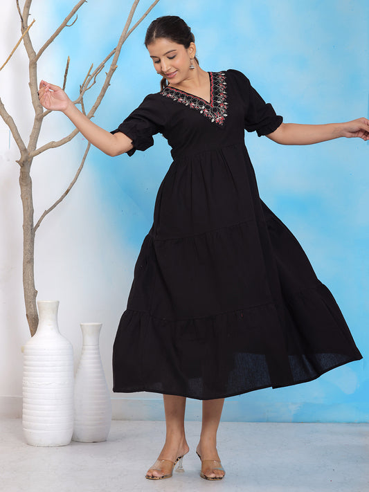 Black embroidered midi dress, V-neck tiered dress, puff sleeve black dress, solid black cotton dress, casual black summer dress, embroidered neckline dress, elegant black midi dress, boho style black dress, 3/4 sleeve A-line dress, festive black dress, flowy solid dress, party wear black midi dress, statement black outfit, embroidered casual dress, ethnic fusion black dress. > Mitrika