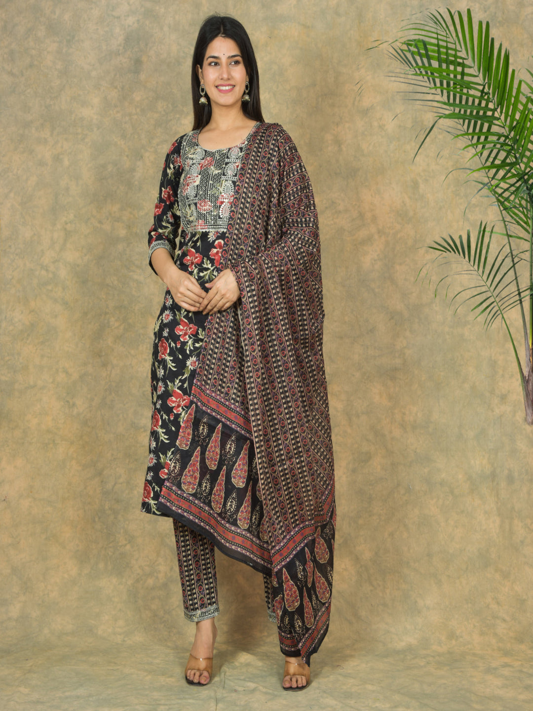 Woman wearing a traditional outfit with a floral pattern against a textured wall.