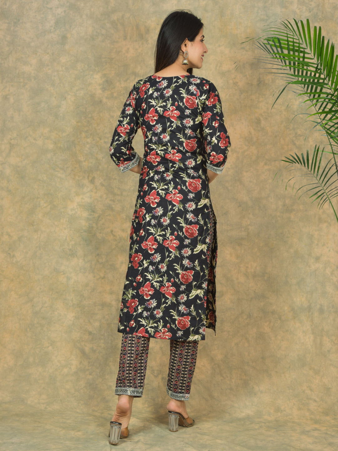 Woman wearing a floral kurta with pants against a textured wall.