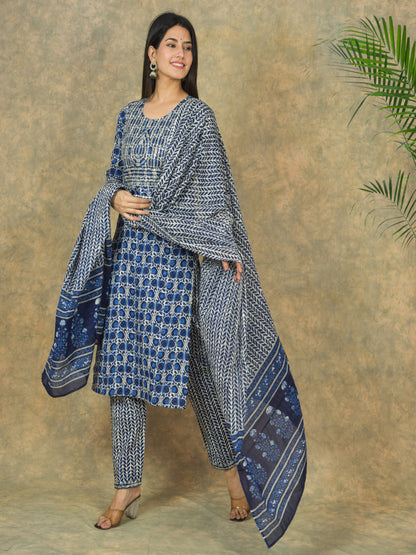Woman wearing a blue and white patterned outfit with a matching shawl against a brown background.