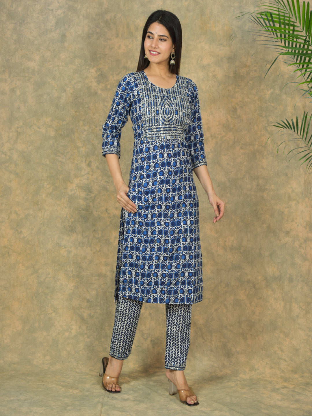 Woman wearing a blue patterned kurta with matching pants against a textured brown background