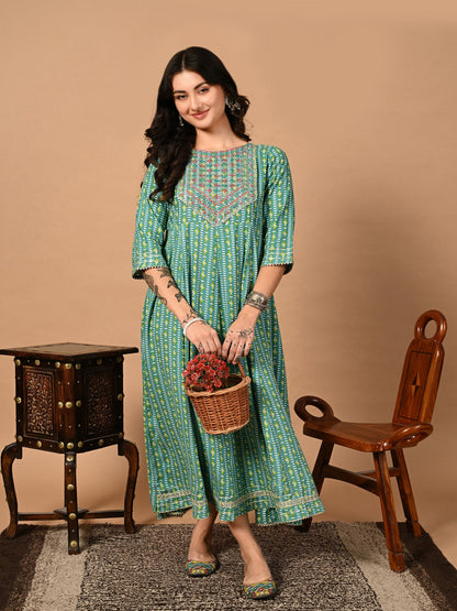 Woman in a green patterned dress holding a basket with flowers against a beige background >Mitrika