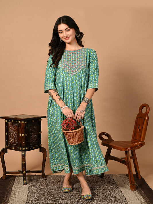 Woman in a green patterned dress holding a basket with flowers against a beige background >Mitrika