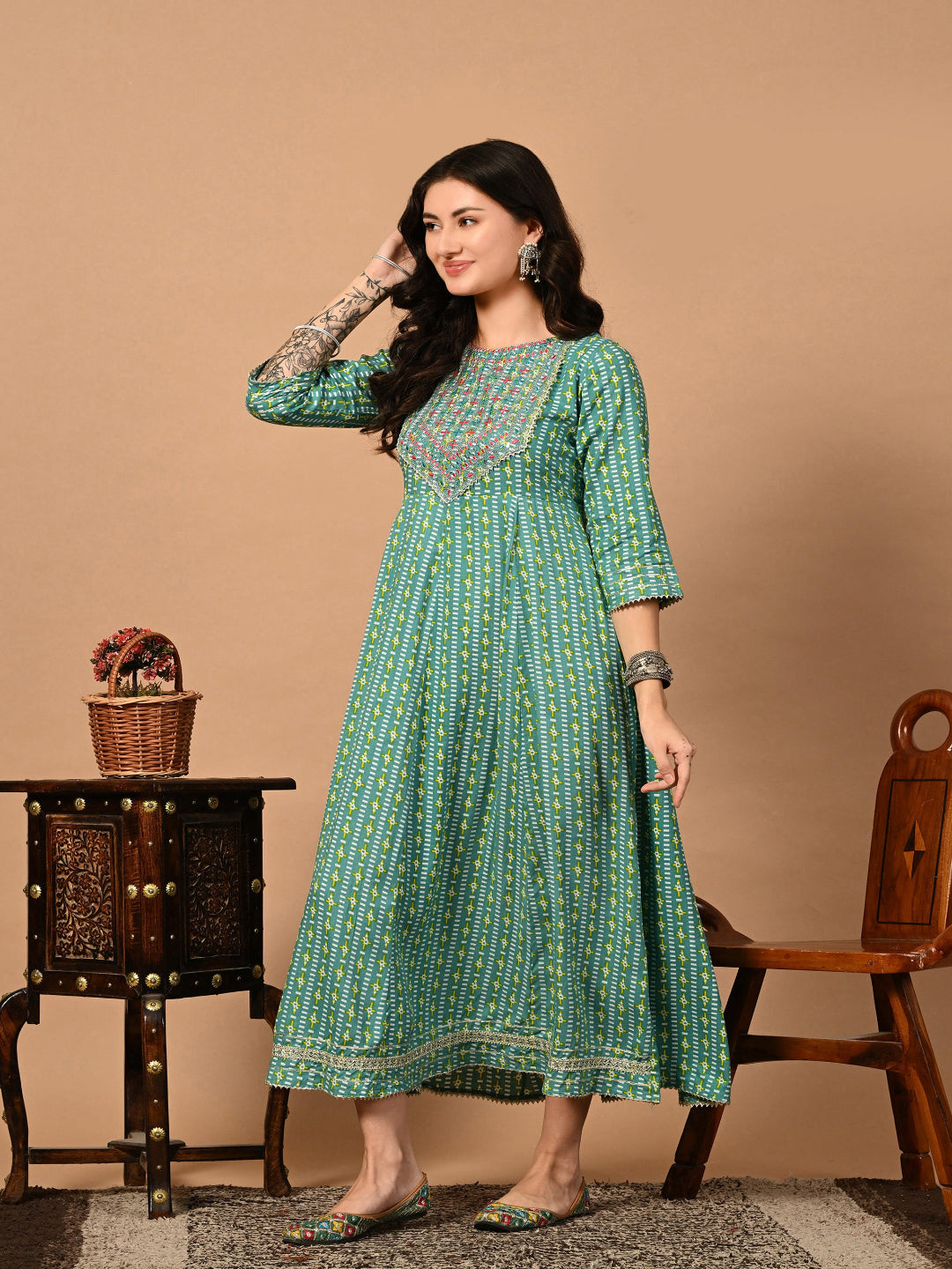 Woman wearing a green patterned dress sitting on a wooden chair against a beige background