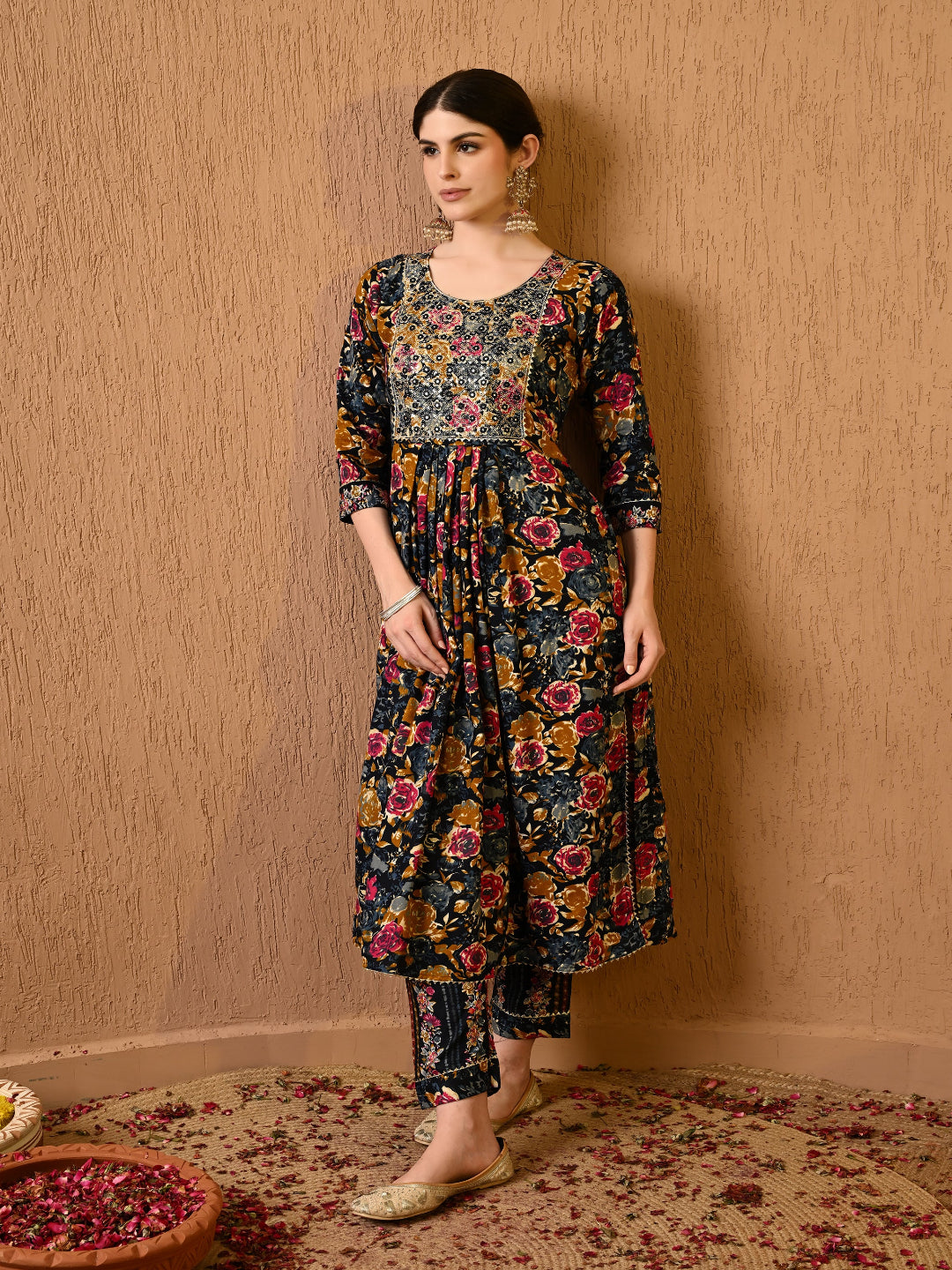 Woman wearing a floral dress and pants against a beige wall.