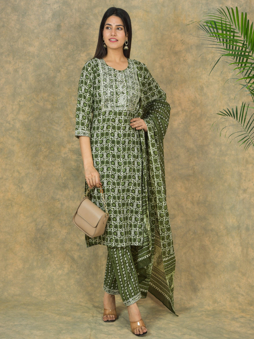 Woman wearing a green patterned outfit with a beige handbag against a textured brown background