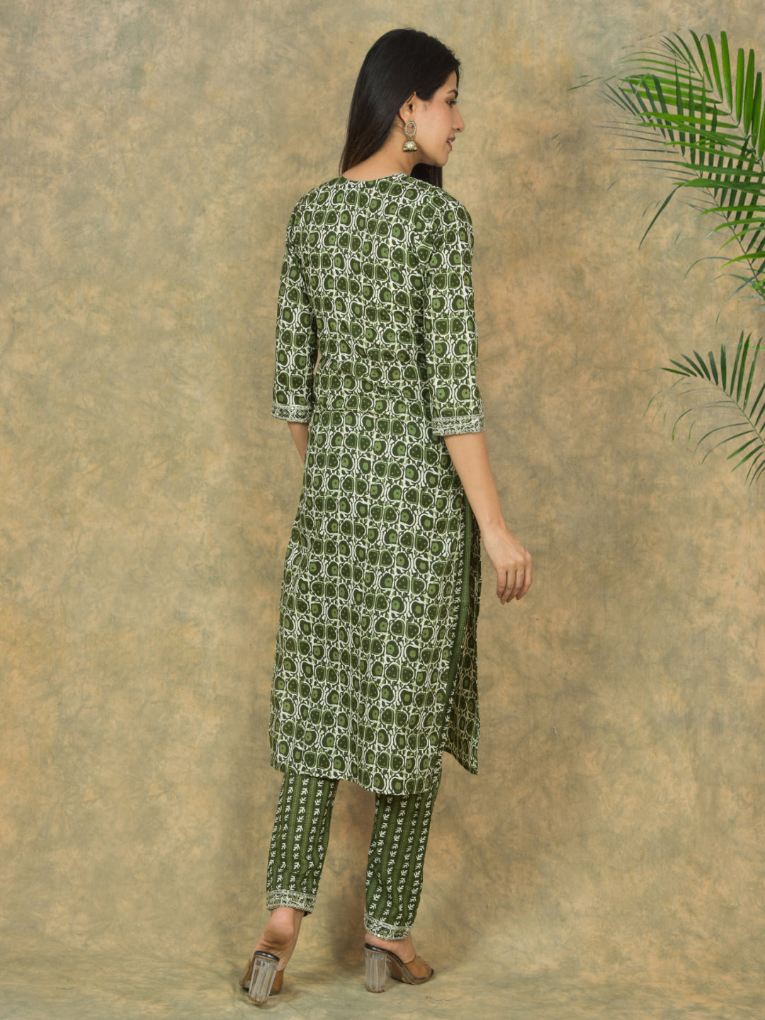 Woman wearing a green patterned kurta with pants against a textured beige background