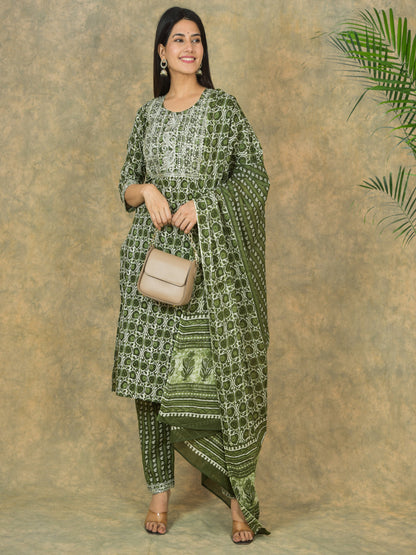 Woman wearing a green patterned outfit with a beige handbag against a textured brown background > Mitrika