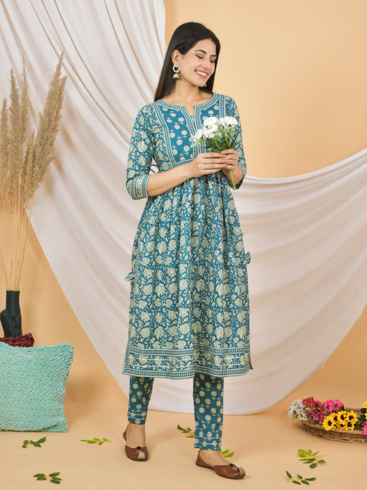 Woman in a blue floral dress holding flowers against a beige background > Mitrika