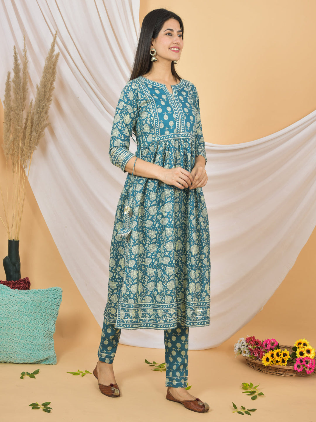Woman wearing a blue floral kurta with pants against a beige and white draped fabric background.
