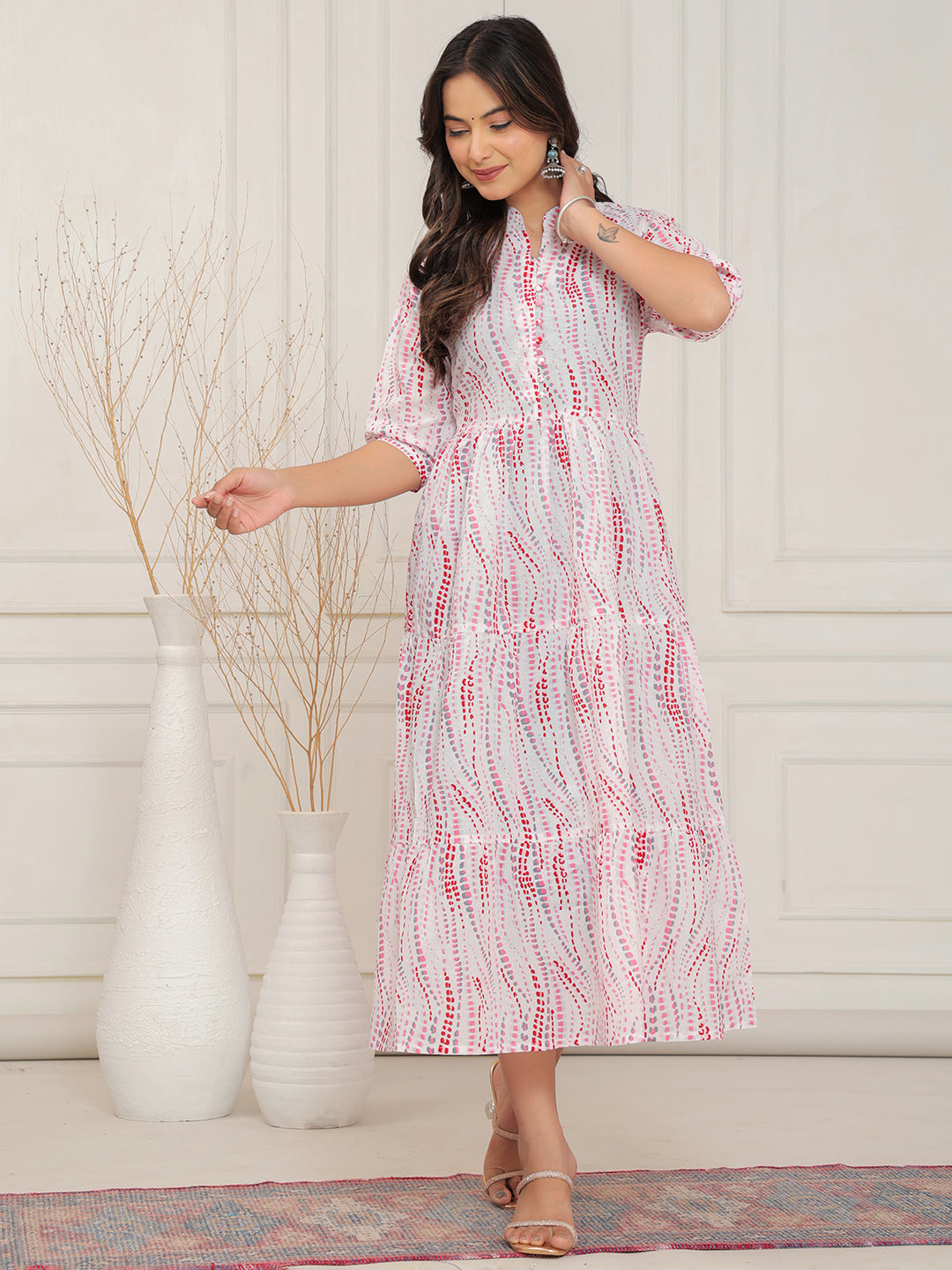 Woman wearing a white dress with red patterns in a room with decorative vases.