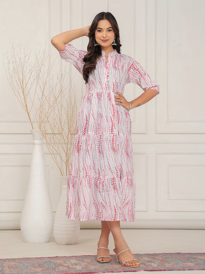 Woman wearing a white dress with red patterns in a room with a white wall and decorative elements.