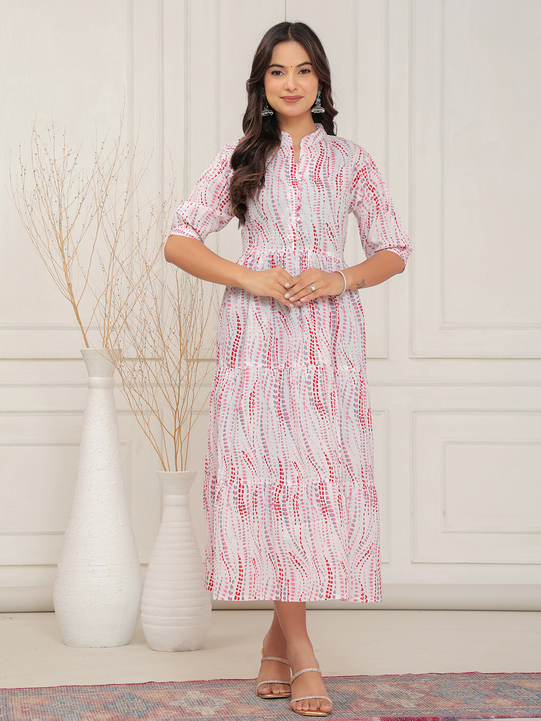 Woman wearing a patterned dress standing in a room with white walls and decorative vases.