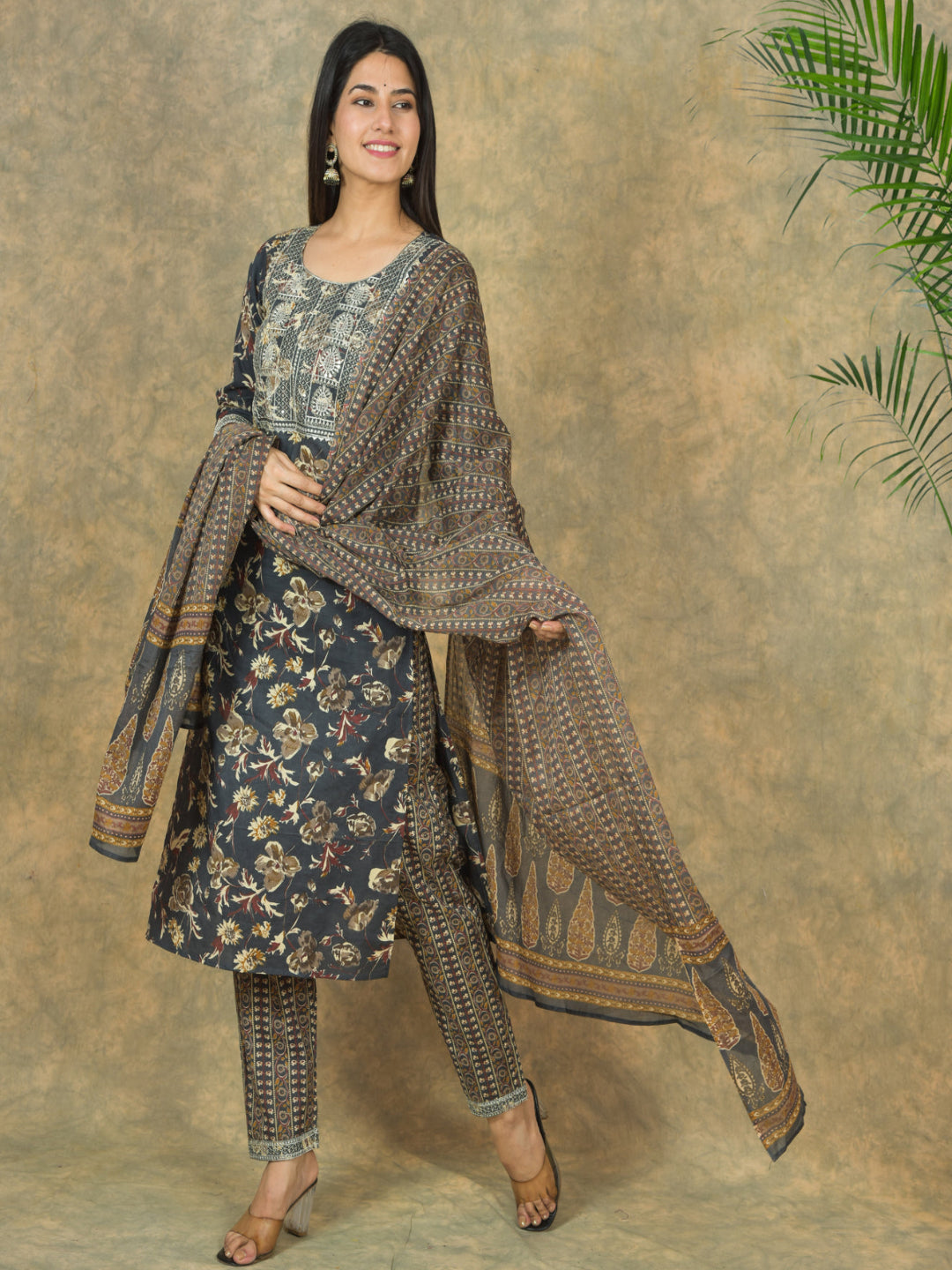 Woman wearing a traditional outfit with a patterned dress and shawl against a textured wall.