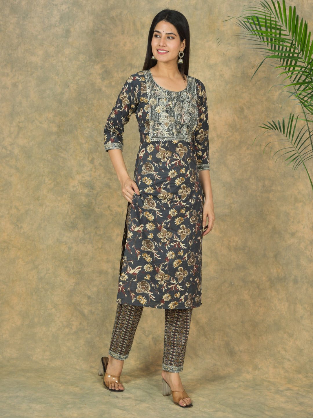 Woman wearing a floral kurta with pants against a textured wall.