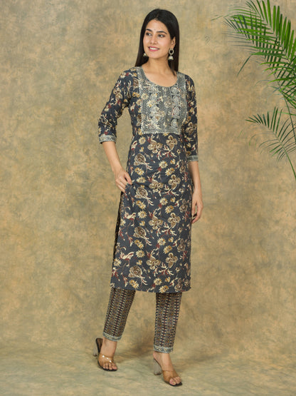 Woman wearing a floral kurta with pants against a textured wall.