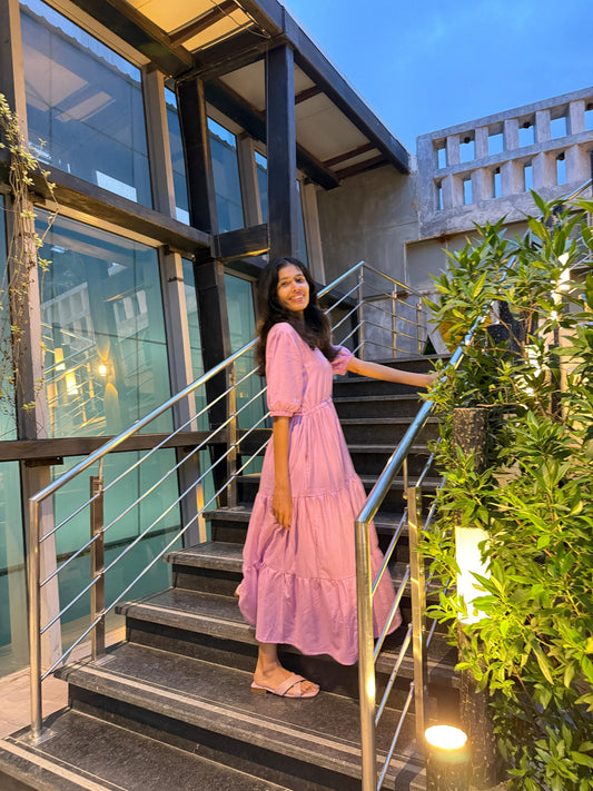 Woman in a pink dress standing on a staircase with modern building and greenery in the background > Mitrika