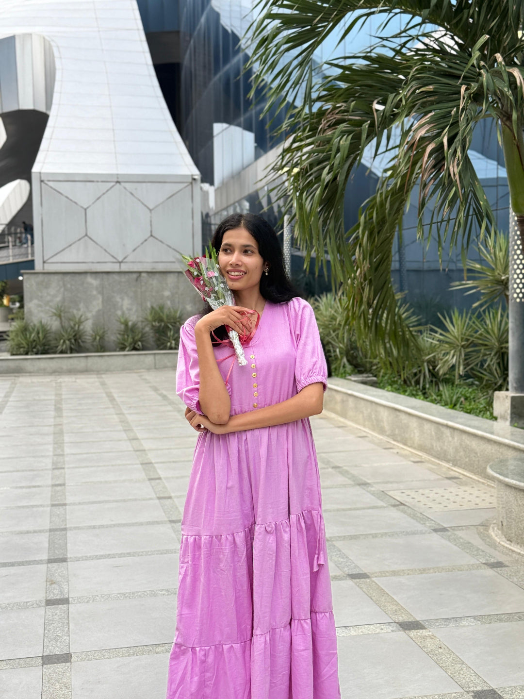 Woman in a pink dress standing outdoors with modern architecture and palm trees in the background