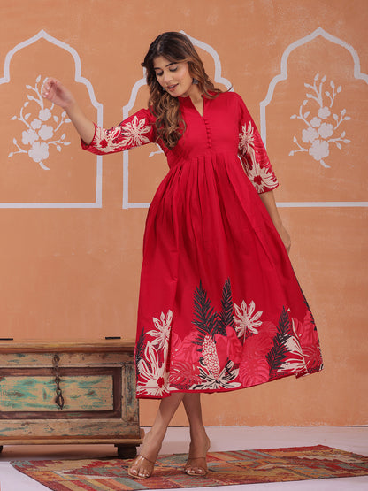Woman wearing a red dress with floral patterns in an indoor setting with decorative wall and wooden chest, Red dress , print dress > Mitrika
