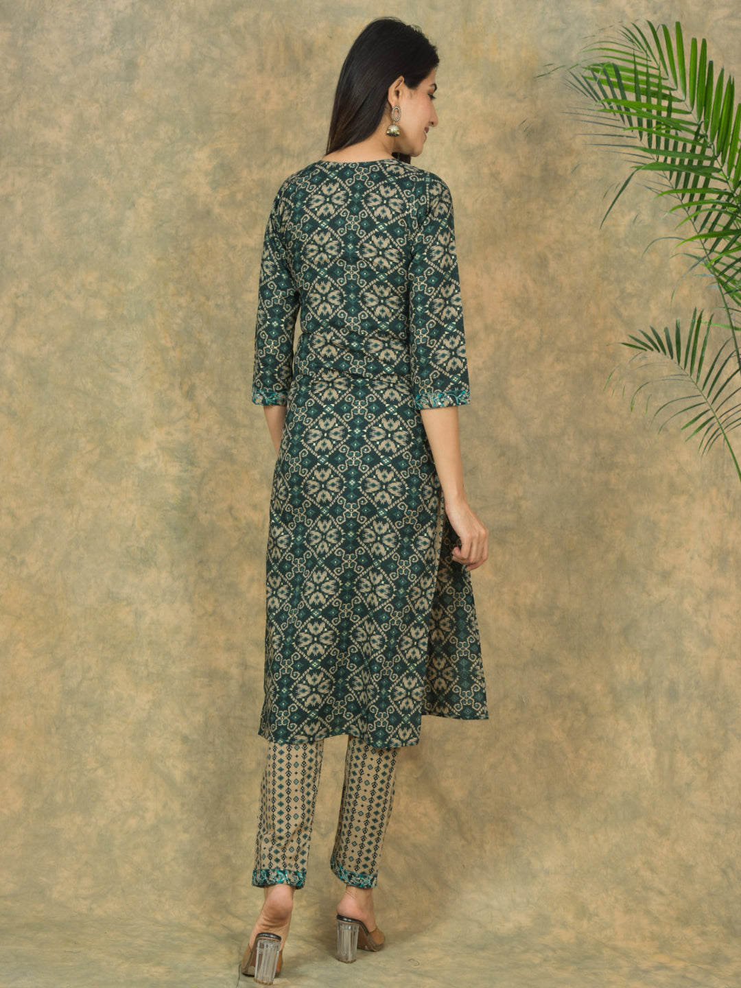 Woman wearing a green patterned kurta with matching pants against a textured beige wall.
