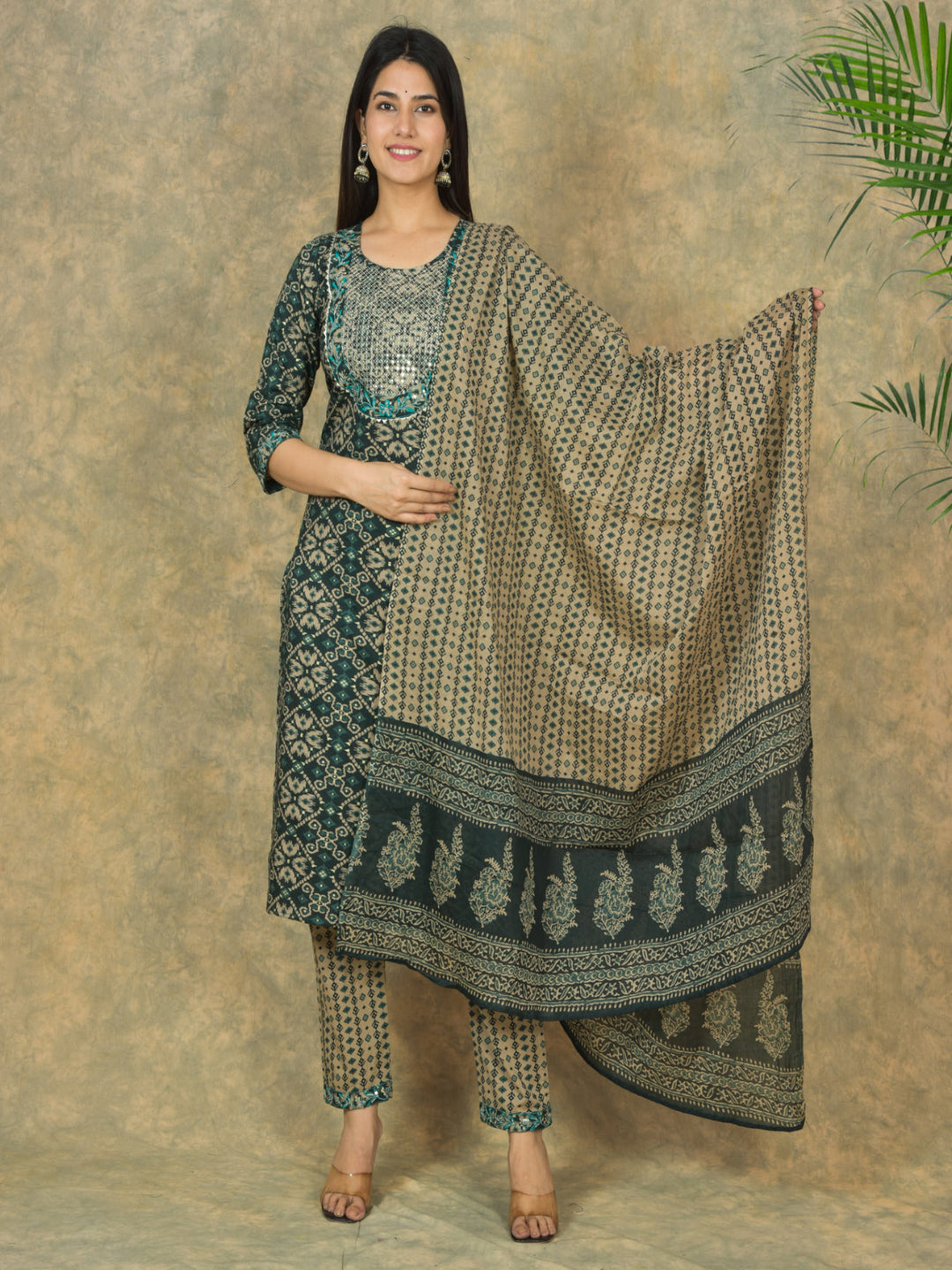 Woman wearing a traditional outfit with a patterned dupatta against a textured wall. > Mitrika