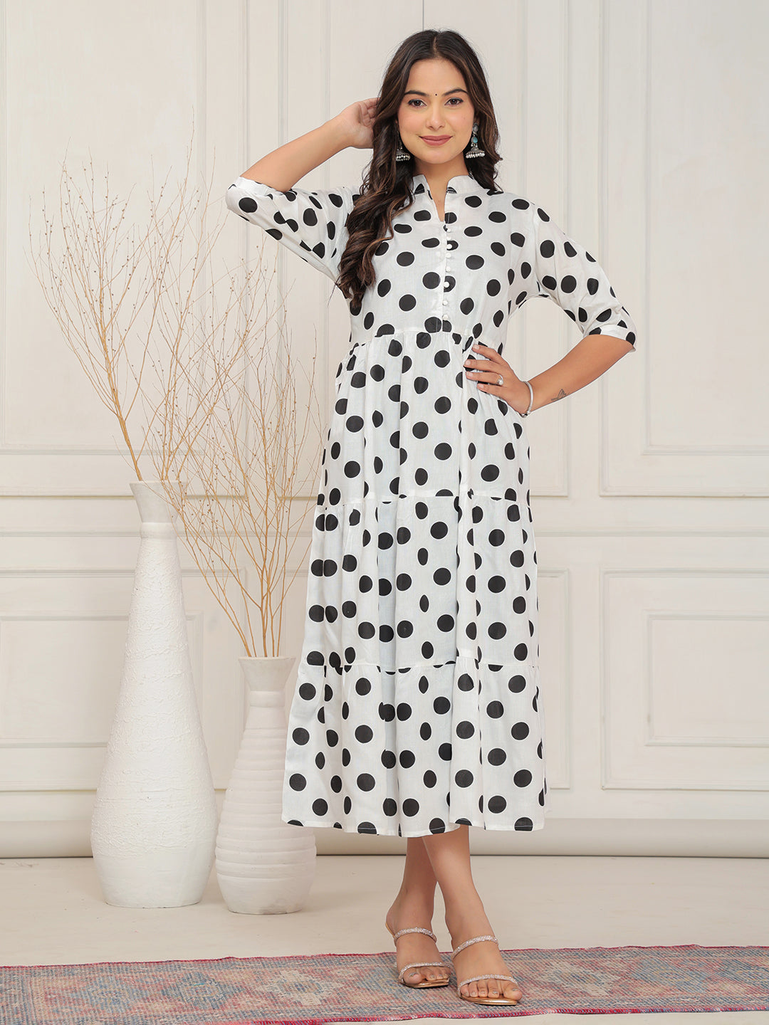 Woman wearing a white dress with black polka dots in a minimalistic setting.