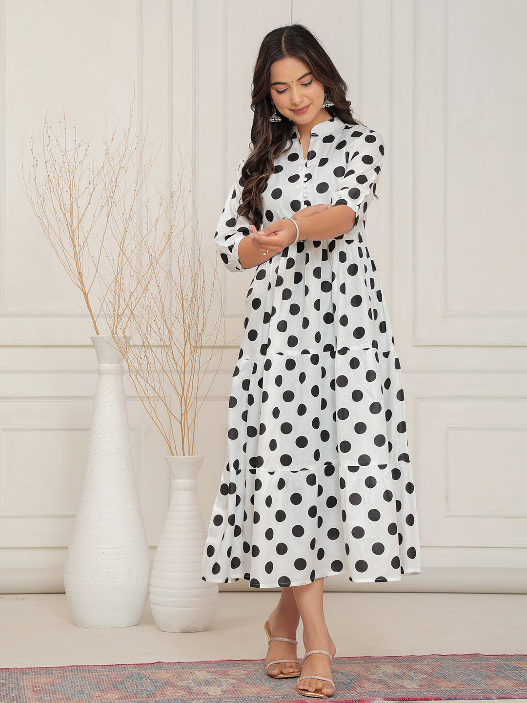 Woman wearing a black and white polka dot dress standing in a room with white walls and decorative vases.