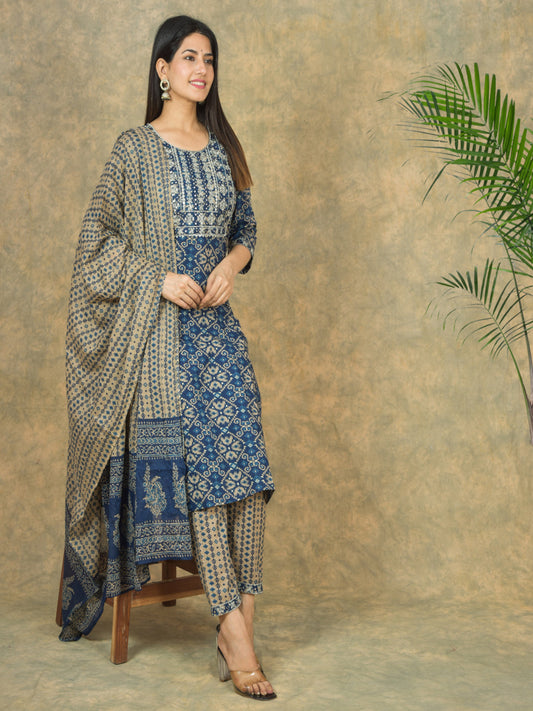 Woman wearing a blue and white patterned outfit with a matching shawl against a textured brown background.