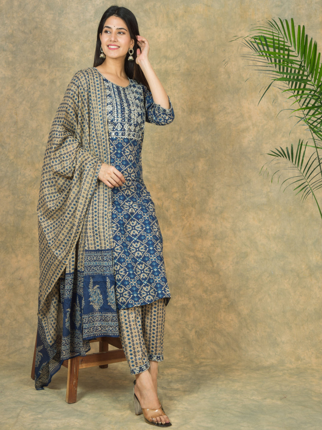 Woman wearing a blue and beige traditional outfit with a plant in the corner